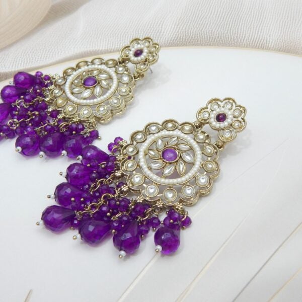 Navratri Purple Jewellery - Royal Reflection DS A pair of large, traditional dangle earrings with a central oval stone, intricate work, a halo of small pearls, and a fan of dangling purple colored beads.