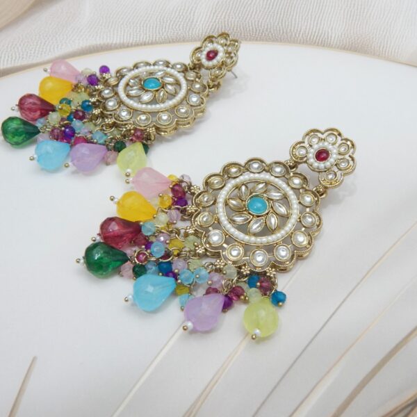 A pair of large, traditional dangle earrings with a central oval stone, intricate work, a halo of small pearls, and a fan of dangling rainbow colored beads.