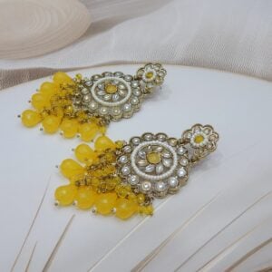 A pair of large, traditional dangle earrings with a central oval stone, intricate work, a halo of small pearls, and a fan of dangling yellow colored beads.