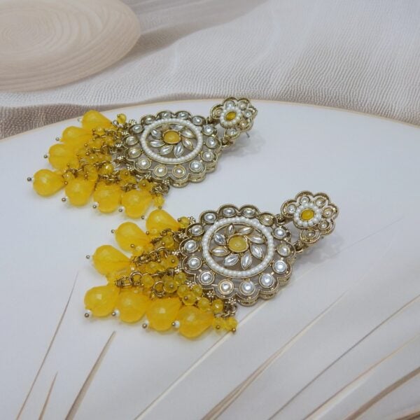 Navratri Yellow Jewellery - Royal Reflection DS A pair of large, traditional dangle earrings with a central oval stone, intricate work, a halo of small pearls, and a fan of dangling yellow colored beads.