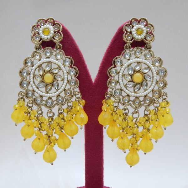 A pair of large, traditional dangle earrings with a central oval stone, intricate work, a halo of small pearls, and a fan of dangling yellow colored beads.