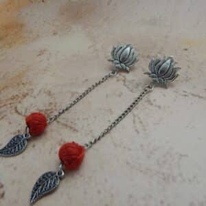 A pair of oxidized silver bohemian earrings featuring a lotus stud, a hanging red woven bead, and a leaf charm