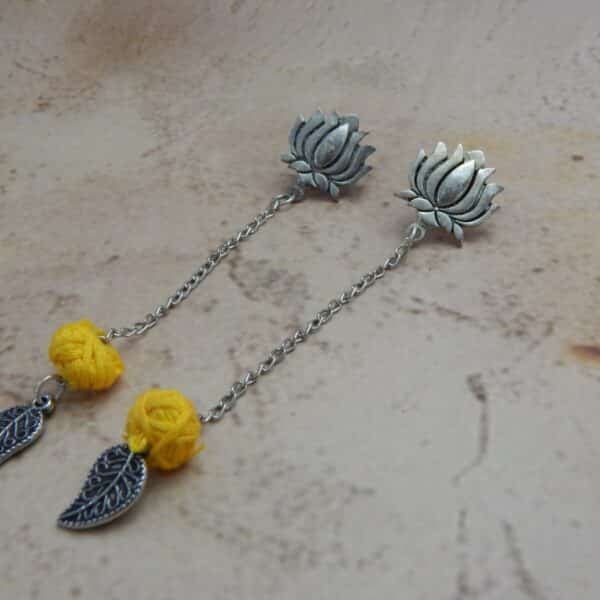 A pair of oxidized silver bohemian earrings featuring a lotus stud, a hanging yellow woven bead, and a leaf charm