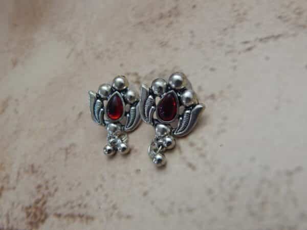 A pair of silver-toned oxidised stud earrings with a lotus flower design, a central red stone, and hanging beaded drops.