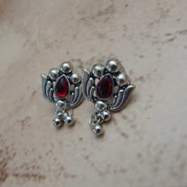 A pair of silver-toned oxidised stud earrings with a lotus flower design, a central red stone, and hanging beaded drops.