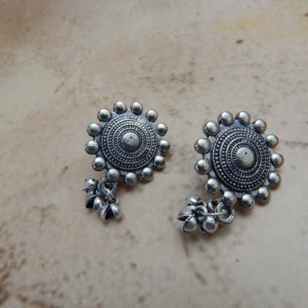 A pair of oxidized silver-toned earrings with a circular mandala-style stud and small jingle bells (ghungroos) dangling from the bottom