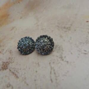 A pair of oxidized silver-toned circular stud earrings with a detailed mandala or star pattern in the center