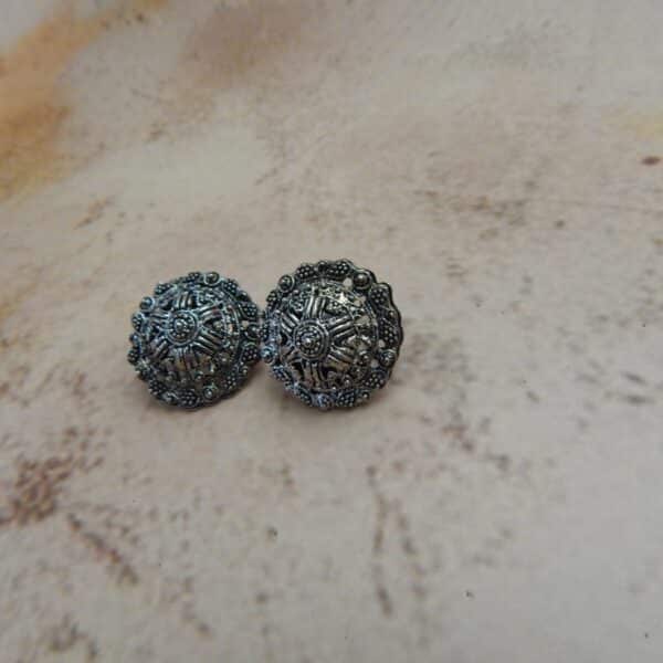 A pair of oxidized silver-toned circular stud earrings with a detailed mandala or star pattern in the center