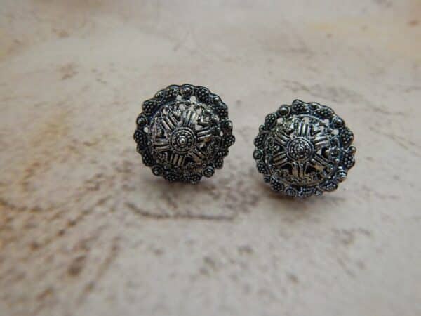 A pair of oxidized silver-toned circular stud earrings with a detailed mandala or star pattern in the center