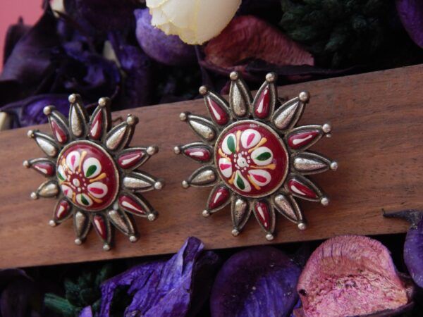 A pair of antique-silver sunburst stud earrings with a colorful Meenakari floral design.