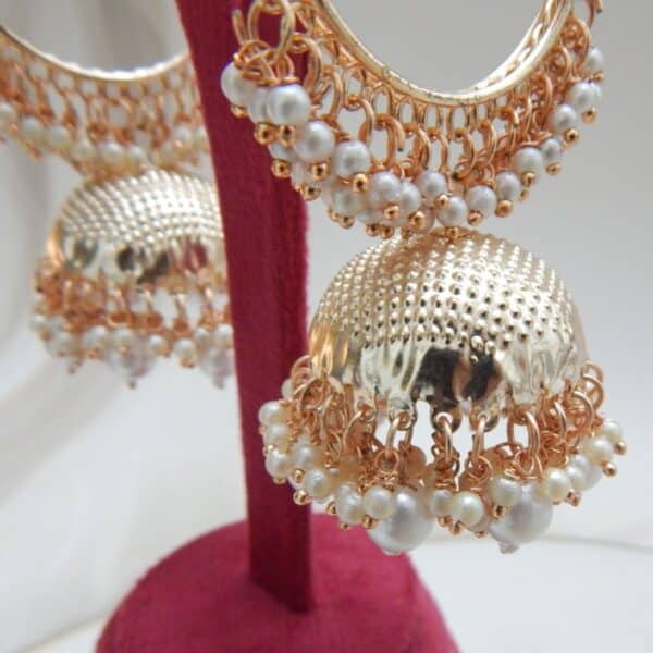 A pair of gold hoop jhumka earrings with white pearls, displayed on a red jewelry stand.