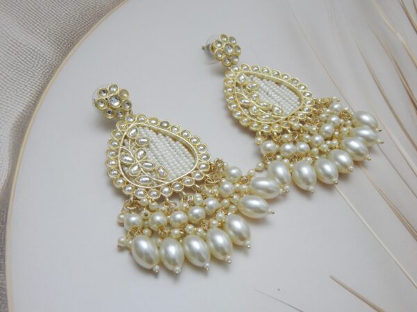 A pair of large, traditional dangle earrings in a teardrop shape with a filigree-like design, covered in small white pearls, and a fan of large pearl drops at the bottom.