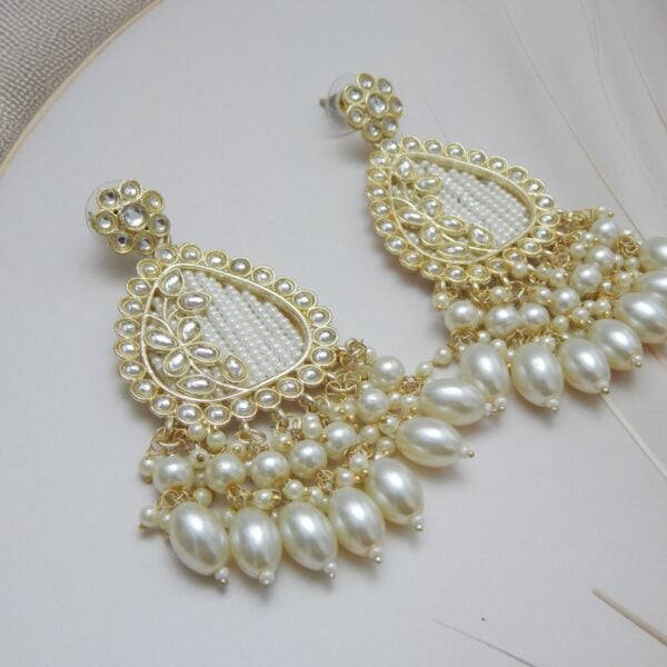 A pair of large, traditional dangle earrings in a teardrop shape with a filigree-like design, covered in small white pearls, and a fan of large pearl drops at the bottom.