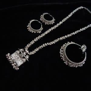 Full German Silver jewelry set featuring a long beaded necklace, an engraved rectangular peacock motif pendant with ghungroos, and matching oxidized jhumka hoops.