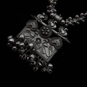 zoom of German Silver jewelry featuring a long beaded necklace, an engraved rectangular peacock motif pendant with ghungroos