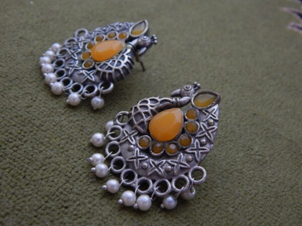 A pair of oxidized silver ethnic earrings with a peacock design, amber stones, and small pearl dangles.