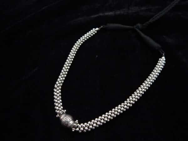 Close-up of a short German Silver oxidized beaded choker necklace featuring a central engraved Dholki-style bead on a black background.