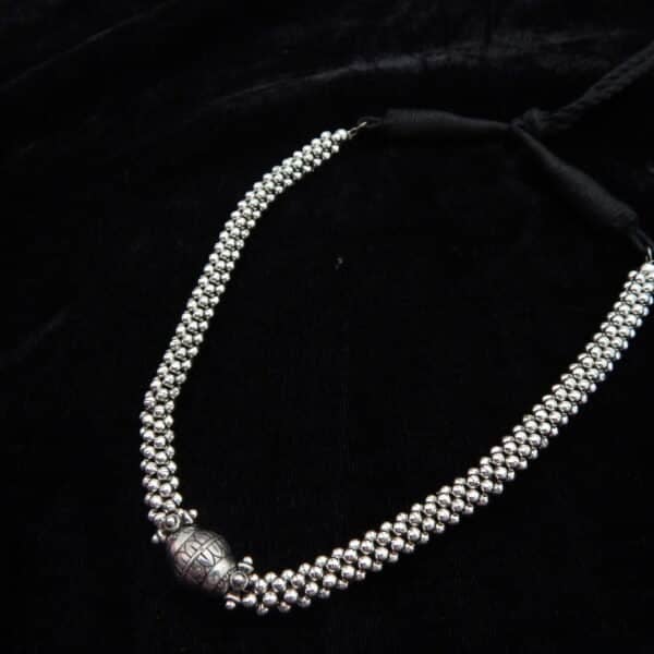 Close-up of a short German Silver oxidized beaded choker necklace featuring a central engraved Dholki-style bead on a black background.