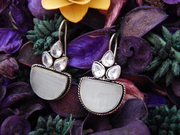 A pair of oxidized silver drop earrings with clear stones and a large, semi-circular milky white/grey opaque stone.