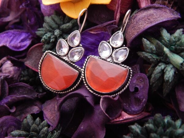 A pair of oxidized silver drop earrings with clear stones and a large, semi-circular red opaque stone.