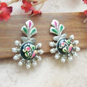 A pair of oxidized silver studs with a floral-shaped top, central green enamel floral work, and pearl bead accents.