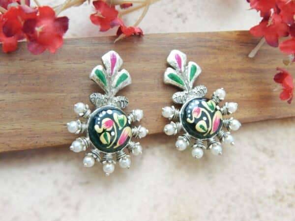 A pair of oxidized silver studs with a floral-shaped top, central green enamel floral work, and pearl bead accents.