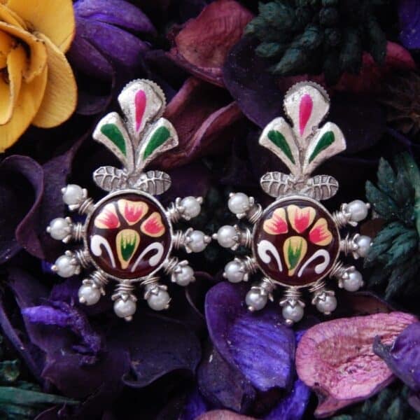 A pair of oxidized silver studs with a floral-shaped top, central maroon enamel floral work, and pearl bead accents.
