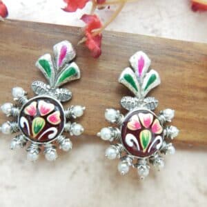 A pair of oxidized silver studs with a floral-shaped top, central green maroon floral work, and pearl bead accents.