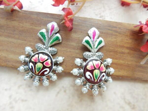 A pair of oxidized silver studs with a floral-shaped top, central green maroon floral work, and pearl bead accents.
