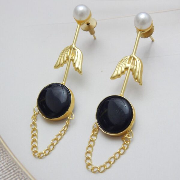 A pair of long gold-tone arrow-design earrings with a pearl stud, a round black colored stone, and a delicate chain loop.