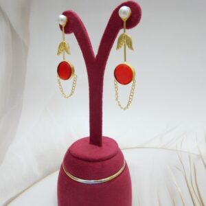 A pair of long gold-tone arrow-design earrings with a pearl stud, a round red colored stone, and a delicate chain loop.