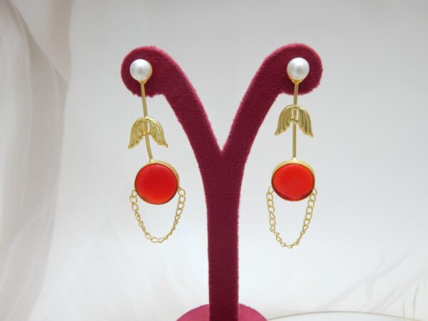 A pair of long gold-tone arrow-design earrings with a pearl stud, a round red colored stone, and a delicate chain loop.