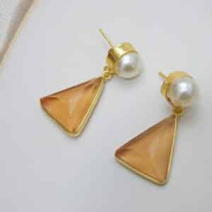 Gold and pearl stud earrings with a dangling, faceted peach-colored triangular stone.