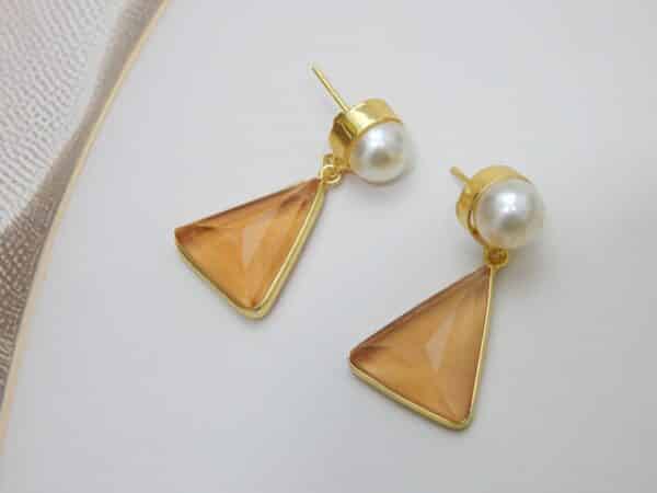 Gold and pearl stud earrings with a dangling, faceted peach-colored triangular stone.