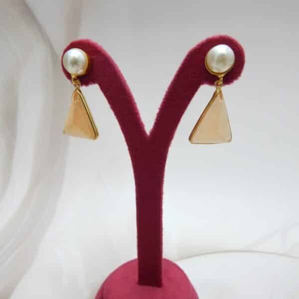 Gold and pearl stud earrings with a dangling, faceted peach-colored triangular stone.