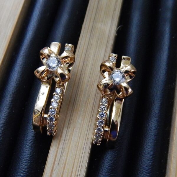A pair of small, gold-plated huggie hoop earrings with a studded ribbon or bow knot design