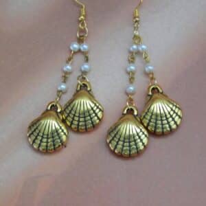 A pair of gold-toned dangle earrings with a chain of small white pearls and two seashell charms hanging from each