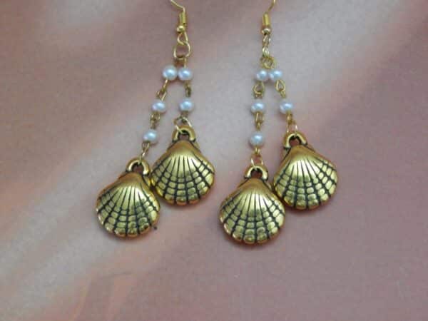 A pair of gold-toned dangle earrings with a chain of small white pearls and two seashell charms hanging from each