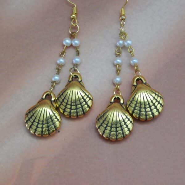 A pair of gold-toned dangle earrings with a chain of small white pearls and two seashell charms hanging from each