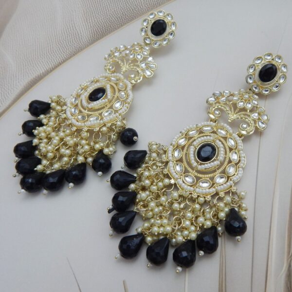 A pair of large, traditional Jhoomar-style Kundan earrings with a central circular stone, surrounded by intricate work and a fan of dangling colored beads and white pearls.