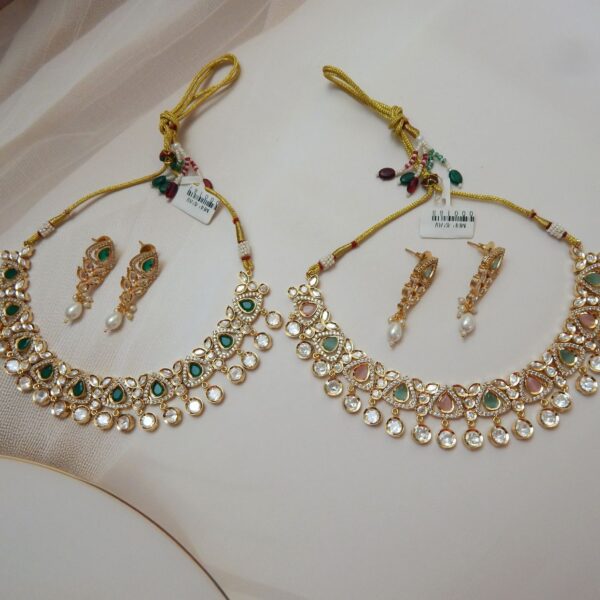 A traditional gold-toned Kundan necklace and earring set with a scalloped design, sparkling clear stones, and pink and green stones.