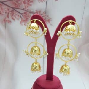 Triple layer jhumka earrings with gold hoops and pearl fringe on a display stand