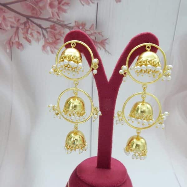 Triple layer jhumka earrings with gold hoops and pearl fringe on a display stand