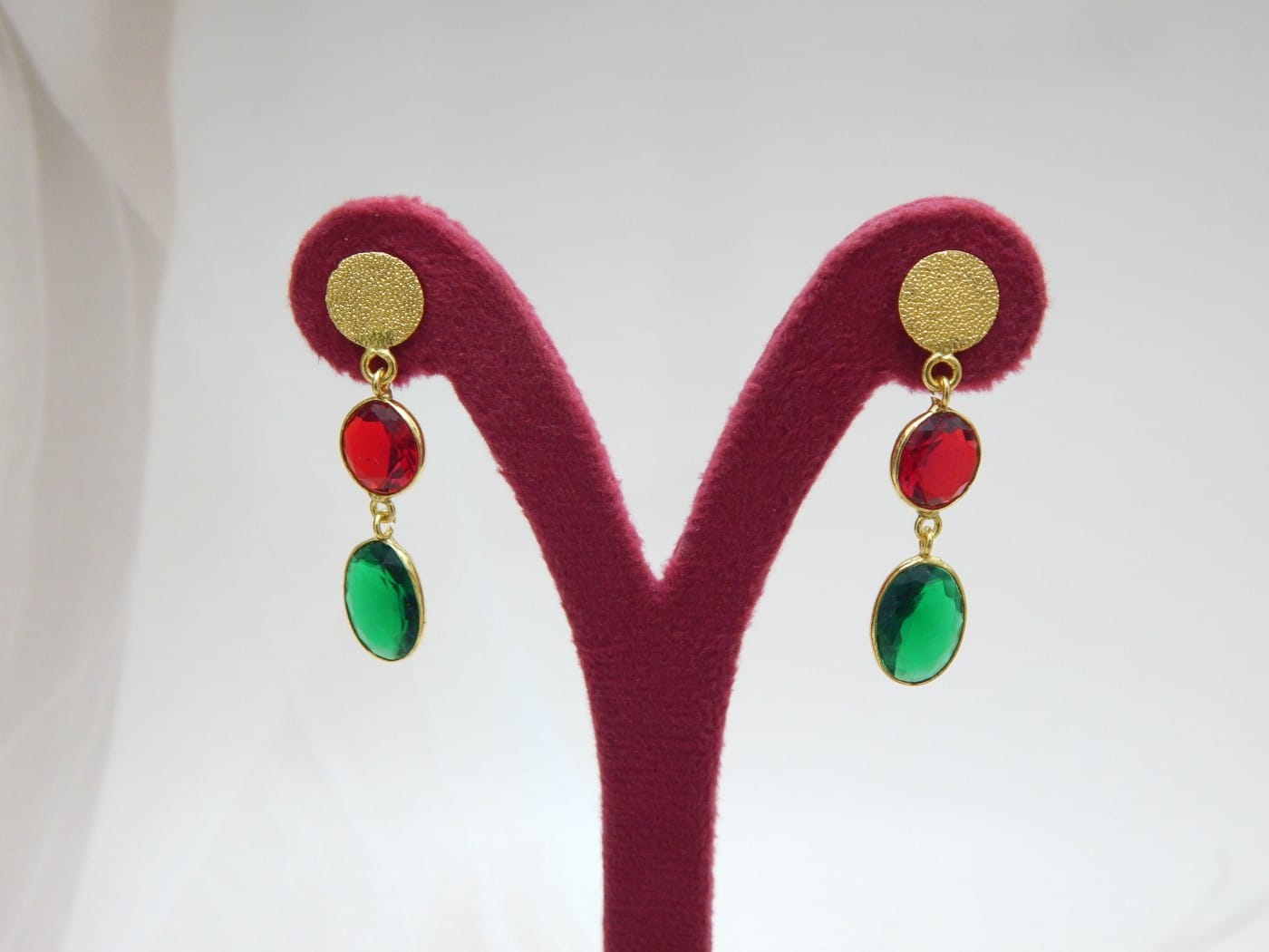 Gold textured stud earrings with a two-stone drop, featuring a round red top stone and an oval dark green stone.