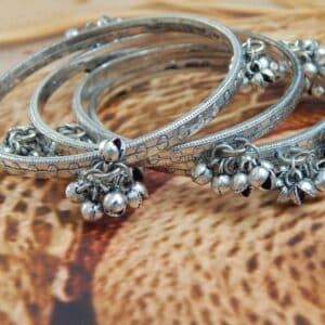 Close-up of four oxidized silver-toned bangles with tribal etching and dangling ghungroo bells, ideal for traditional and college wear.