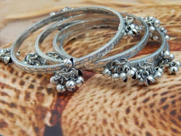 Close-up of four oxidized silver-toned bangles with tribal etching and dangling ghungroo bells, ideal for traditional and college wear.