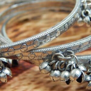 zoom of four oxidized silver-toned bangles with tribal etching and dangling ghungroo bells, ideal for traditional and college wear.