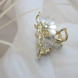 vertical view of Small gold-toned hair claw clip with clear rhinestones and opalescent white/off-white cat-eye flower petals, elegant hair accessory for women.