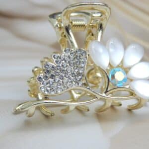 Small gold-toned hair claw clip with clear rhinestones and opalescent white/off-white cat-eye flower petals, elegant hair accessory for women.