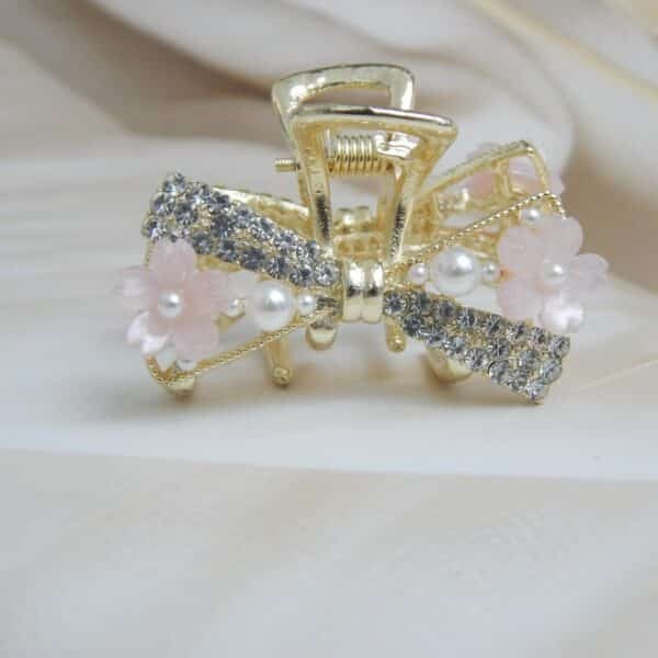 Navratri Purple Jewellery - Royal Reflection DS Small gold-toned hair claw clip with a crystal bow, pearl beads, and small pink resin flowers, elegant hair accessory for women.